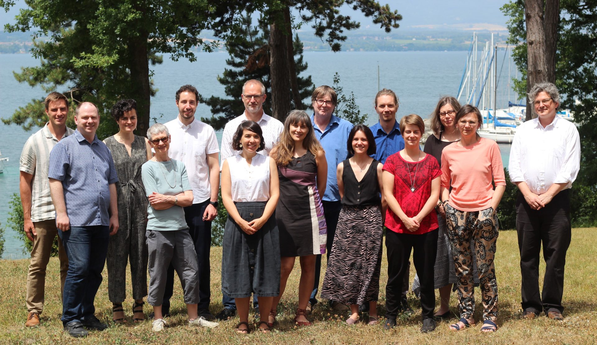 15 members of the itDf team pose for a group photograph on the lake shire, with tress and boats seen in the background. There are 7 males and 8 females.