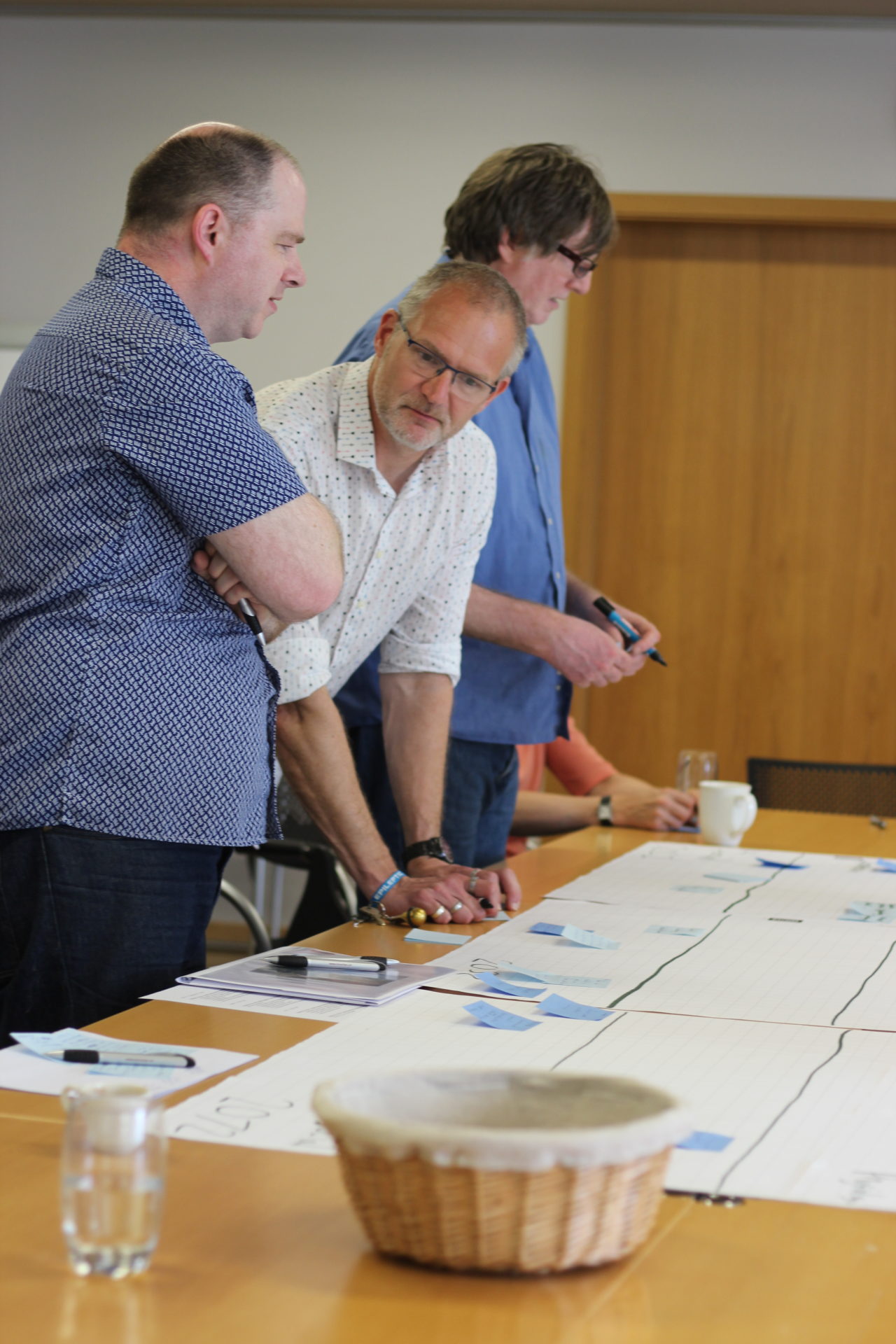 Ray Holt and Stuart Murray muse over the implications of the drawn timeline. They stand at a table looking at papers spread out on the table top (Tony Prescott in the background).