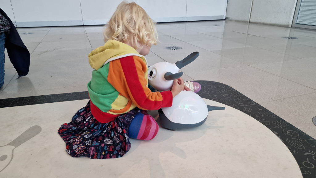 a young girl is sat on the floor embracing a Miro robot 