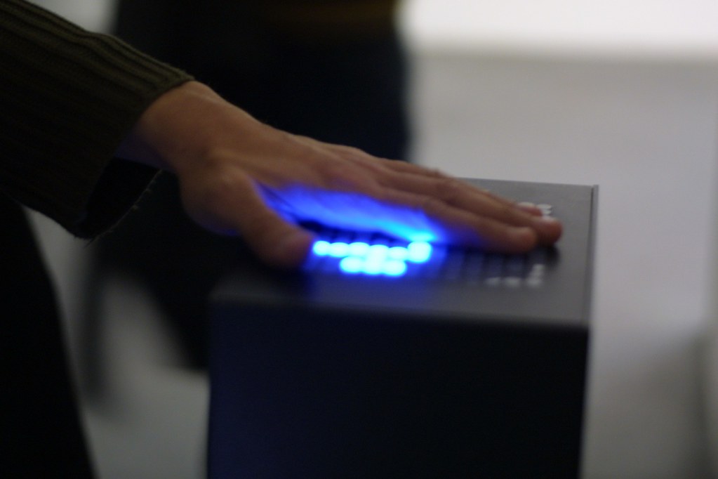 A person's left hand is resting on a haptic device with blue LEDs.