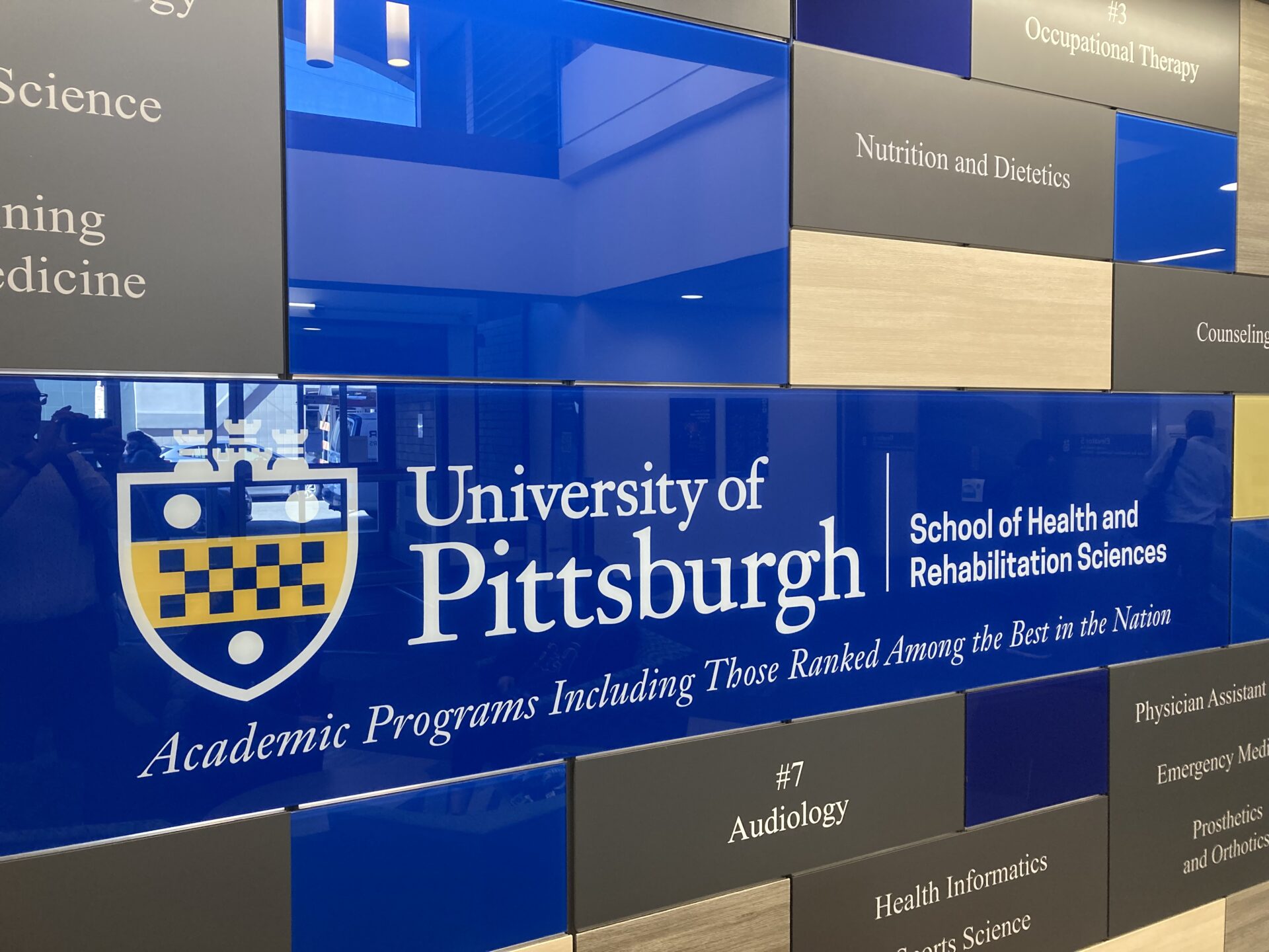 A sign inside University building that reads ‘University of Pittsburgh: School of Health and Rehabilitation Sciences’ and displays the University crest